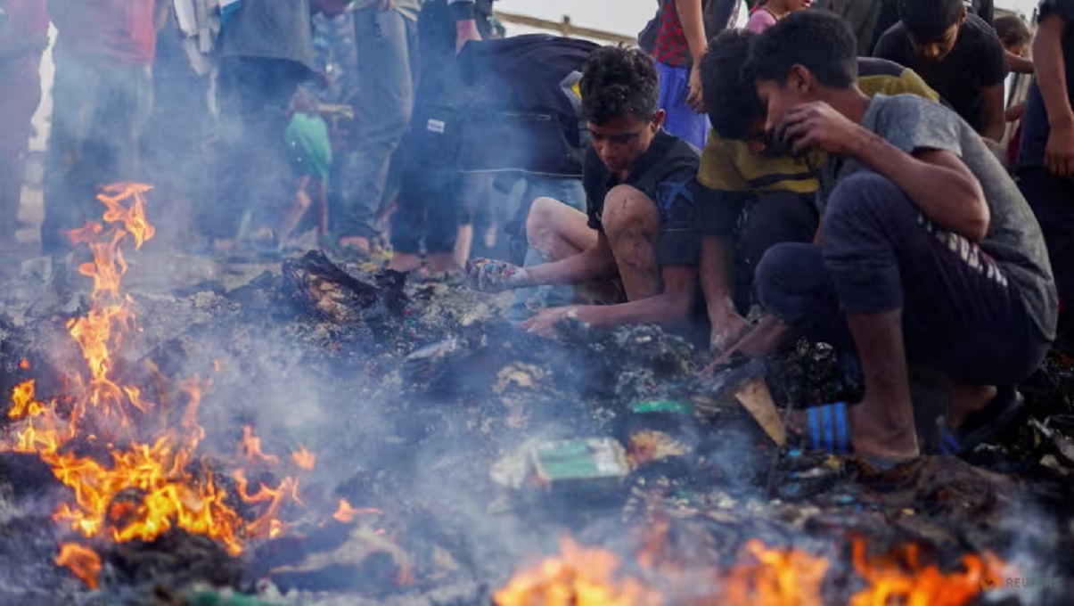 Palestinians search for food among burnt debris in the aftermath of an Israeli strike on an area designated for displaced people in Rafah, in the southern Gaza Strip.